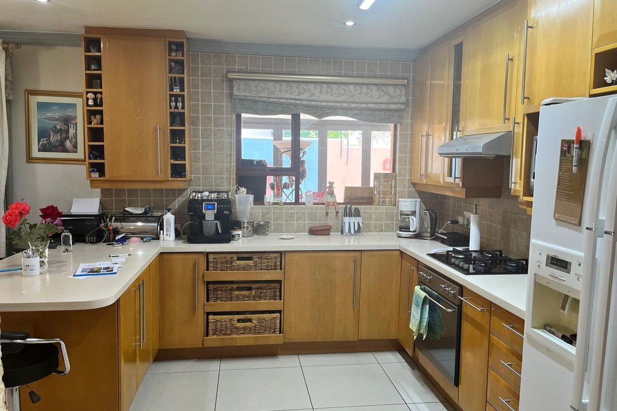 A functional U-shaped kitchen featuring light wood cabinetry, stone-look countertops, a built-in oven, gas hob, and tiled flooring.