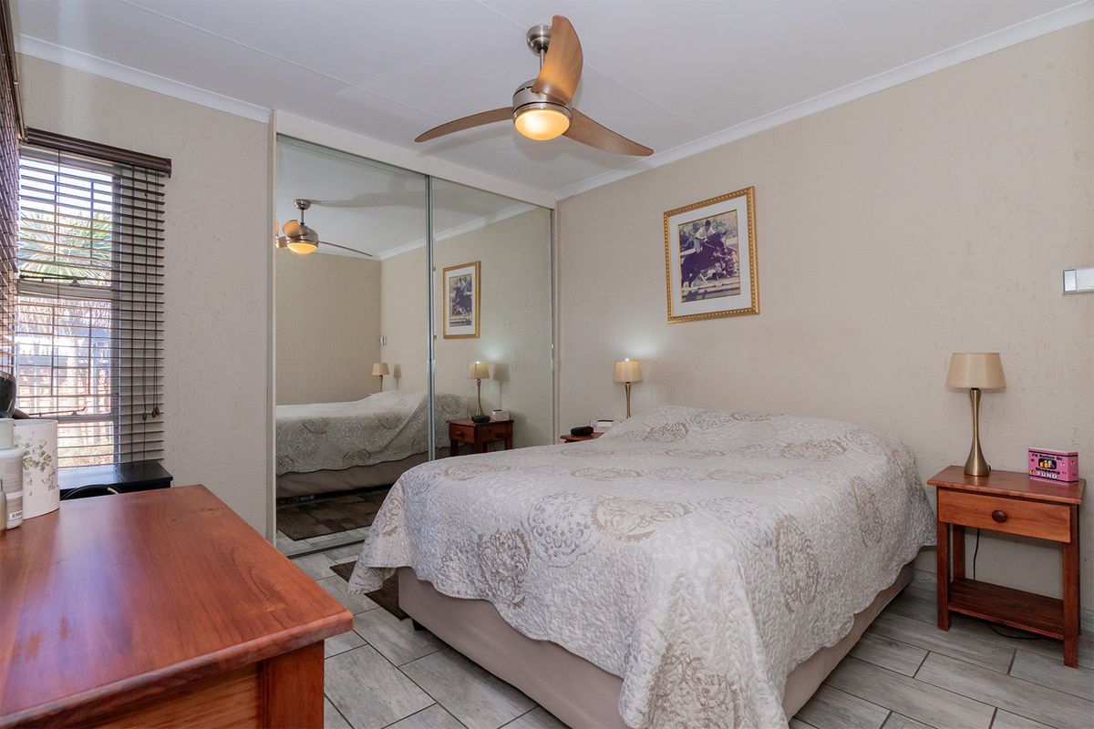 A bedroom featuring tiled flooring, a ceiling fan, and built-in mirrored sliding door cupboards.