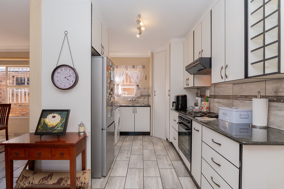 A functional galley-style kitchen featuring white cabinetry, dark granite countertops, a built-in oven with extractor fan, and tiled flooring.