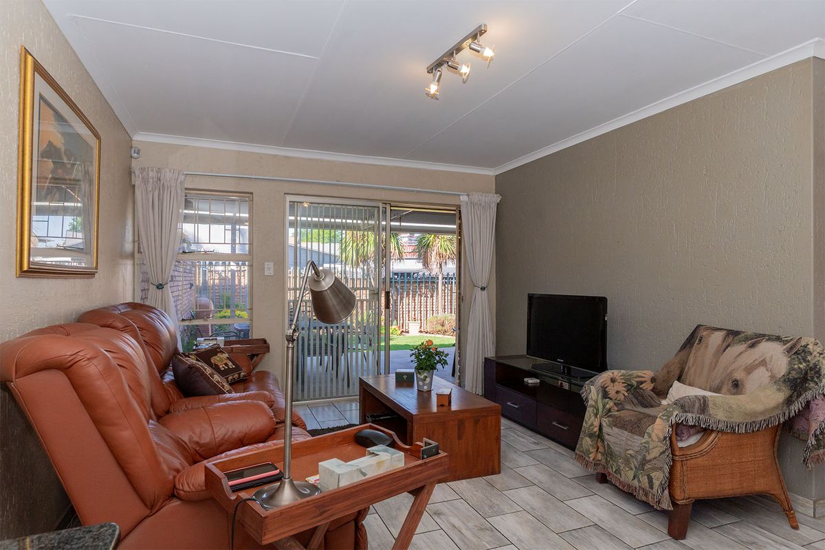 A comfortable living room featuring tiled flooring, a ceiling-mounted spotlight fixture, and sliding glass doors providing direct access to the rear patio and garden.