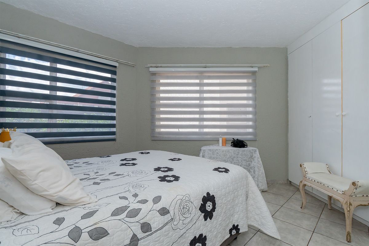 A bedroom featuring tiled flooring, built-in wardrobe storage, and dual zebra blinds for adjustable natural light.