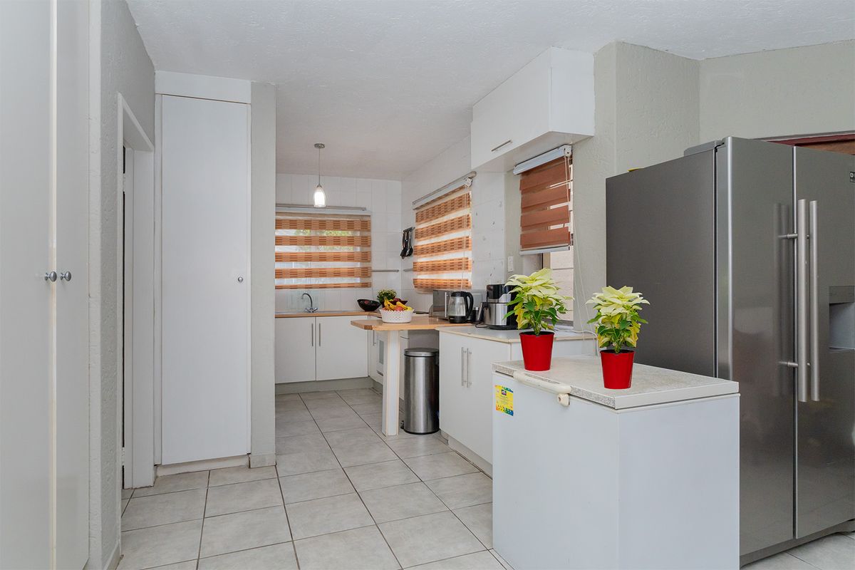 A functional kitchen featuring white built-in cabinetry, tiled flooring, a stainless steel sink, and a tiled backsplash with ample natural light.