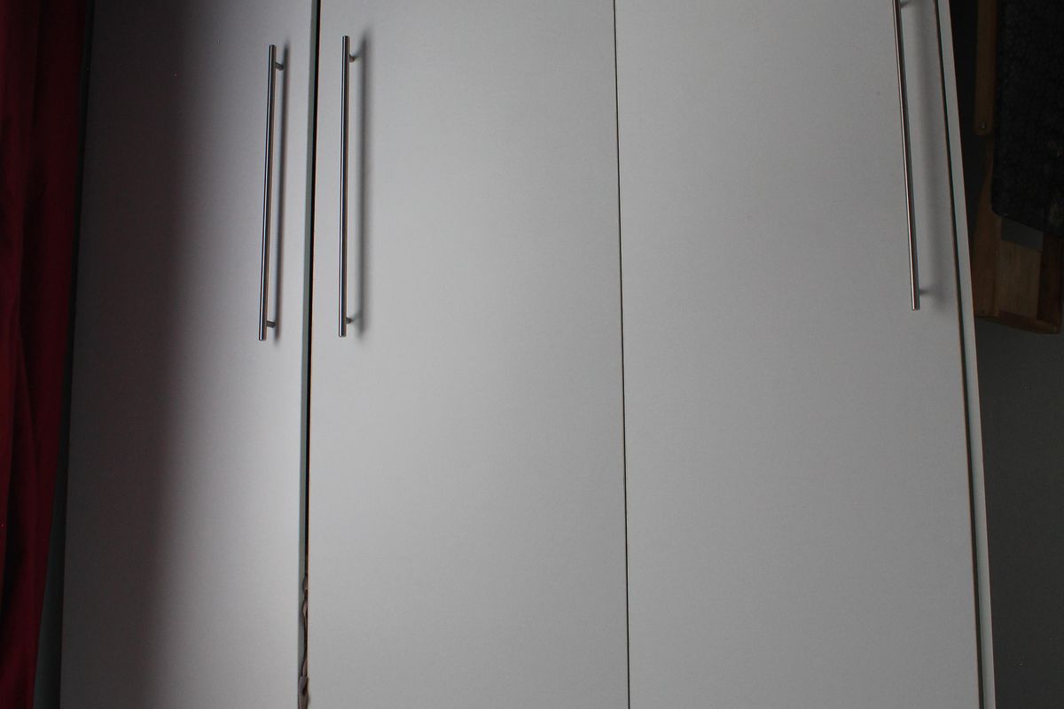 A white built-in wardrobe featuring modern metal handles, providing ample storage space within the bedroom.