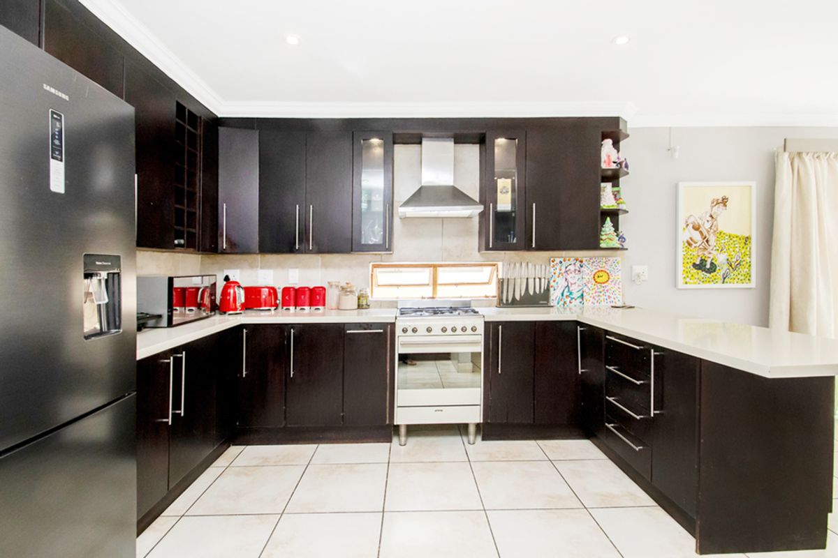 A functional kitchen featuring dark cabinetry, stone countertops, a stainless steel extractor fan, and a freestanding gas stove with oven.