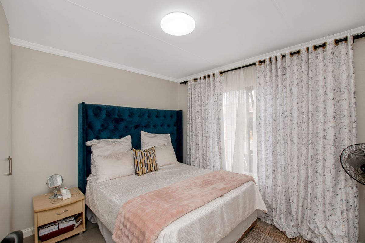 A well-maintained bedroom featuring neutral wall tones, crown molding, and a large window dressed with floor-to-ceiling curtains.