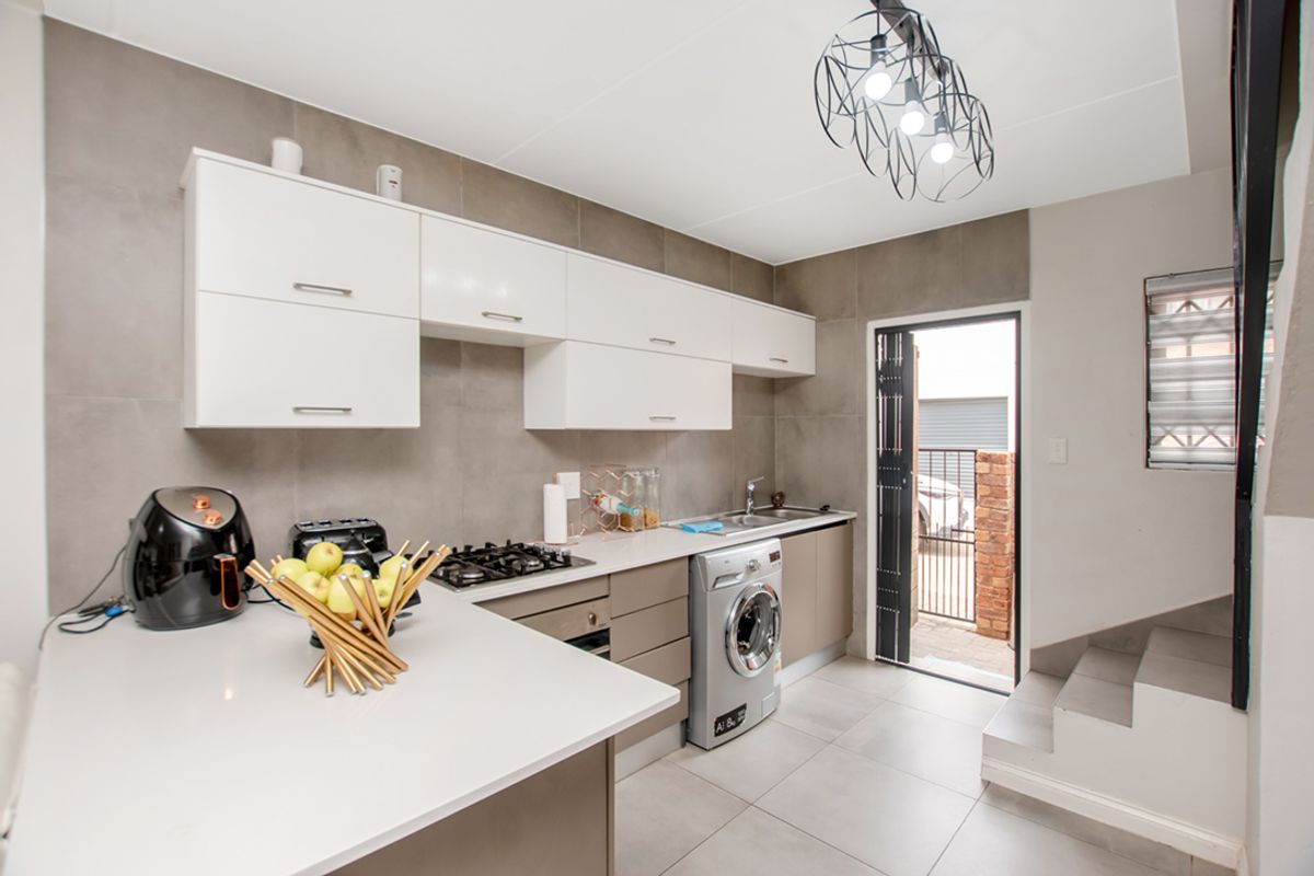 Modern kitchen featuring sleek white cabinetry, stone countertops, integrated gas hob, and tiled flooring, with direct access to an outdoor area.