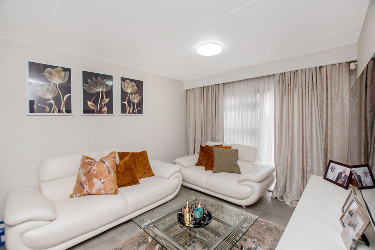 A well-maintained living room featuring neutral wall tones, tiled flooring, and floor-to-ceiling curtains providing access to natural light.