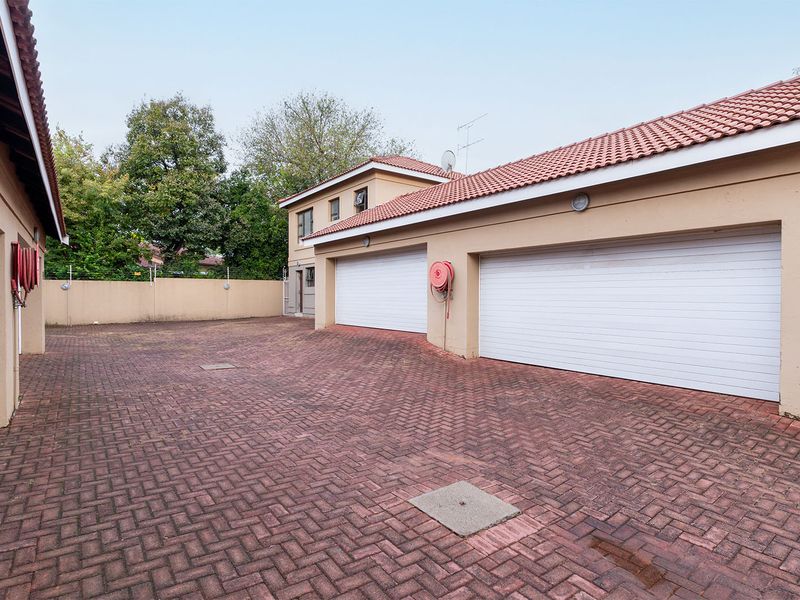 A spacious paved driveway area featuring a double garage with white roller doors and perimeter walling.