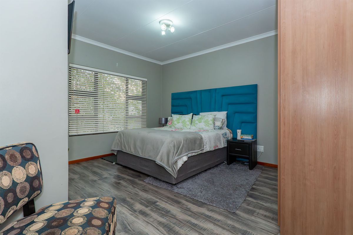 A well-maintained bedroom featuring modern laminate flooring, a built-in wardrobe, and venetian blinds, offering a comfortable and functional living space.