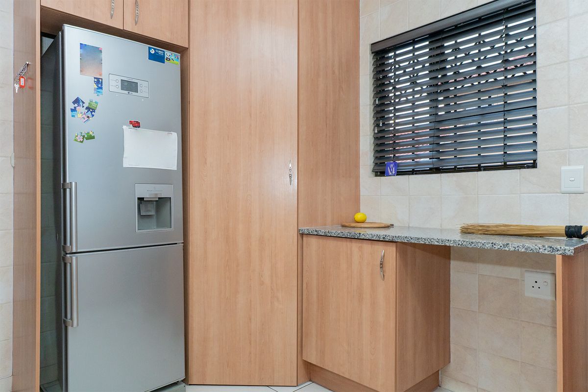 A functional kitchen area featuring light wood-finish cabinetry, granite countertops, and a tiled backsplash with a window fitted with venetian blinds.