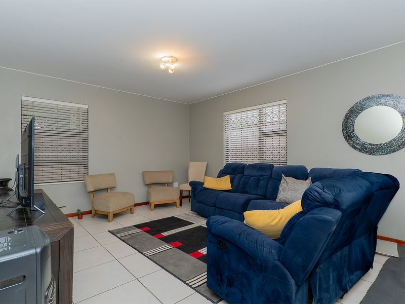A comfortable living room featuring neutral wall tones, tiled flooring, and large windows fitted with venetian blinds.