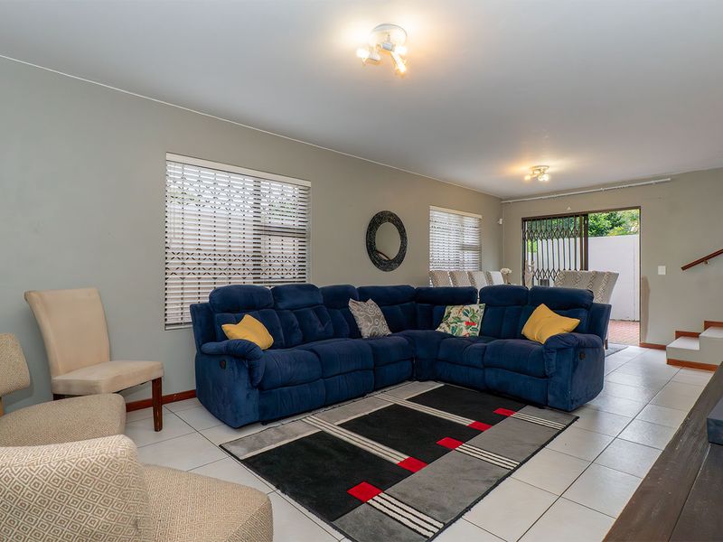Spacious living area featuring neutral tiled flooring, large windows with venetian blinds, and direct access to an outdoor patio through a sliding glass door.