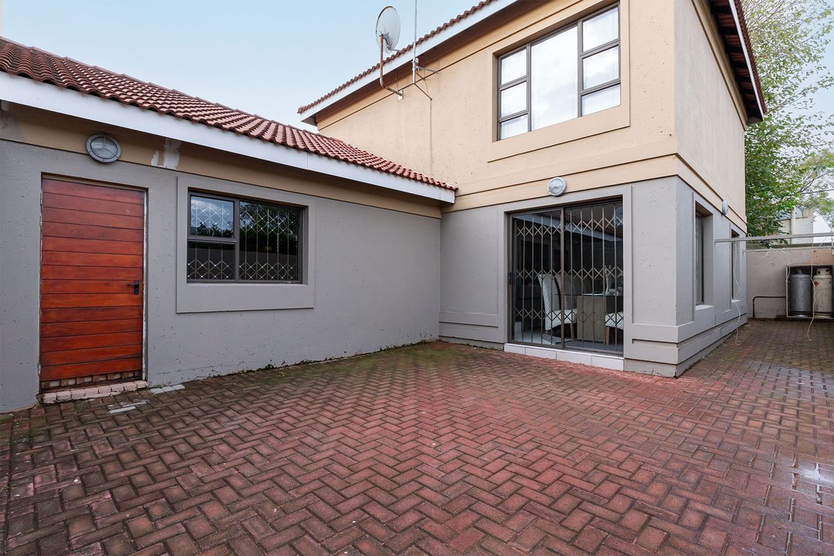 Rear exterior view featuring brick paved courtyard, sliding glass door with security gate, and timber access door to the side of the house.