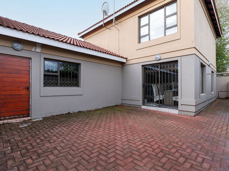 Rear exterior view featuring brick paved courtyard, sliding glass door with security gate, and timber access door to the side of the house.