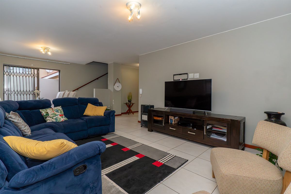 A spacious living room featuring tiled flooring, neutral wall tones, and direct access to an outdoor area through a security gate.