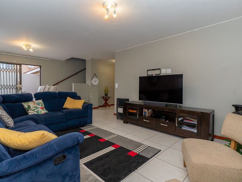 A spacious living room featuring tiled flooring, neutral wall tones, and direct access to an outdoor area through a security gate.