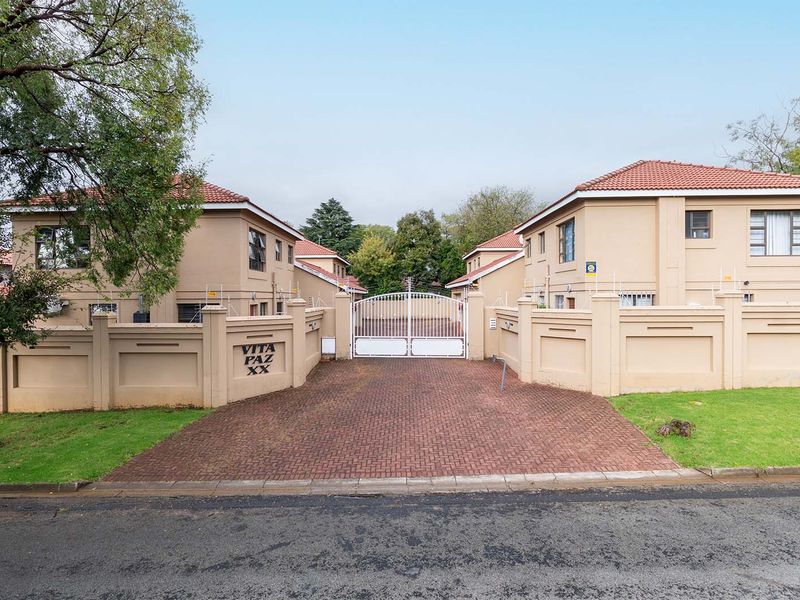 Front view of the Vita Paz XX residential complex featuring a secure gated entrance, brick paved driveway, and perimeter wall with electric fencing.