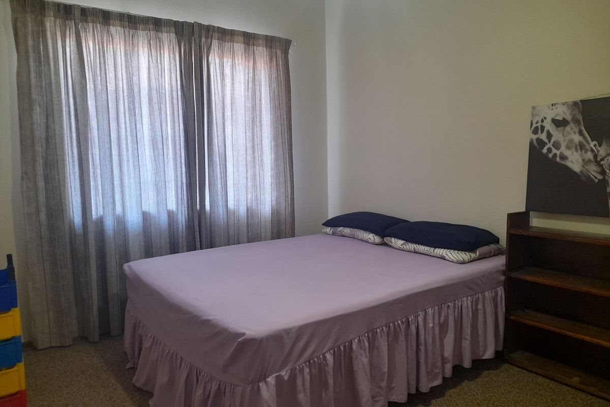A standard bedroom featuring neutral wall finishes, carpeted flooring, and a window fitted with curtain tracks.
