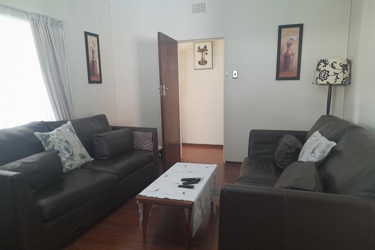 A living room featuring laminate wood flooring, neutral wall finishes, and a doorway leading to an adjacent room.