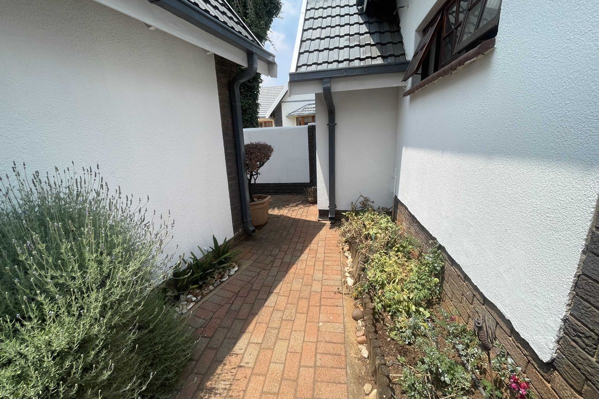 A paved exterior walkway between two sections of the house, featuring brick pathways and established garden borders.