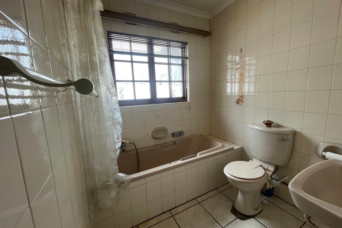 A dated bathroom featuring a built-in bathtub, standard toilet, and wall-mounted basin with full-height wall tiling.