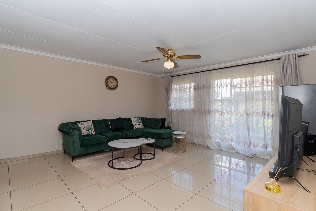 A bright living room featuring large windows with sheer curtains, tiled flooring, and a ceiling fan, offering a comfortable and functional living space.