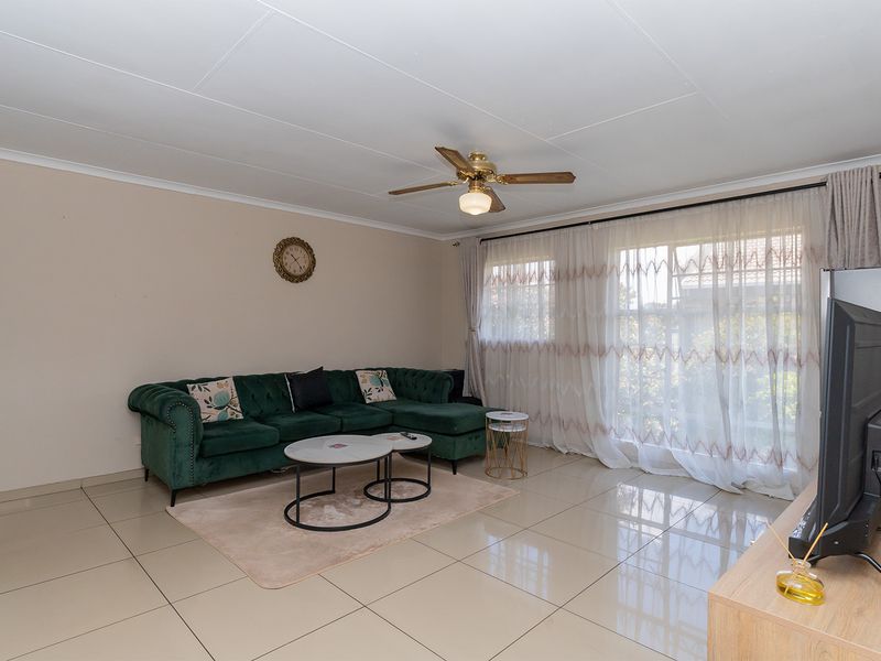 A bright living room featuring large windows with sheer curtains, tiled flooring, and a ceiling fan, offering a comfortable and functional living space.