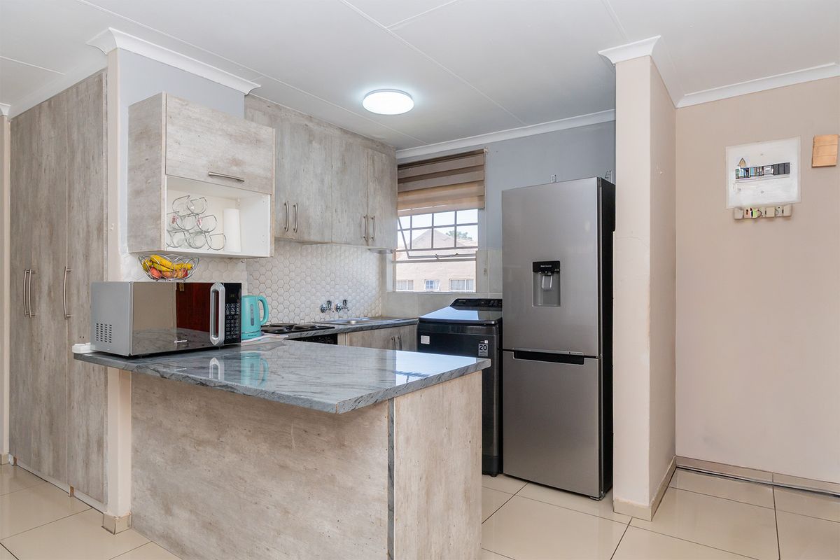 Modern kitchen featuring light wood-look cabinetry, stone-effect countertops, a breakfast bar, and tiled flooring in an open-plan layout.
