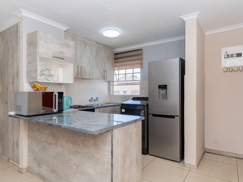 Modern kitchen featuring light wood-look cabinetry, stone-effect countertops, a breakfast bar, and tiled flooring in an open-plan layout.