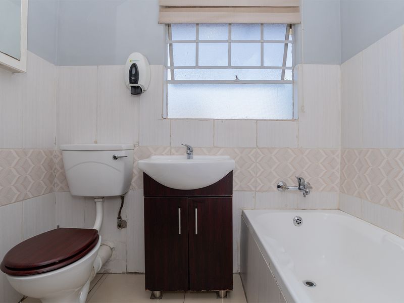 A functional bathroom featuring a bathtub, vanity basin, and toilet with tiled walls and a window for natural light.