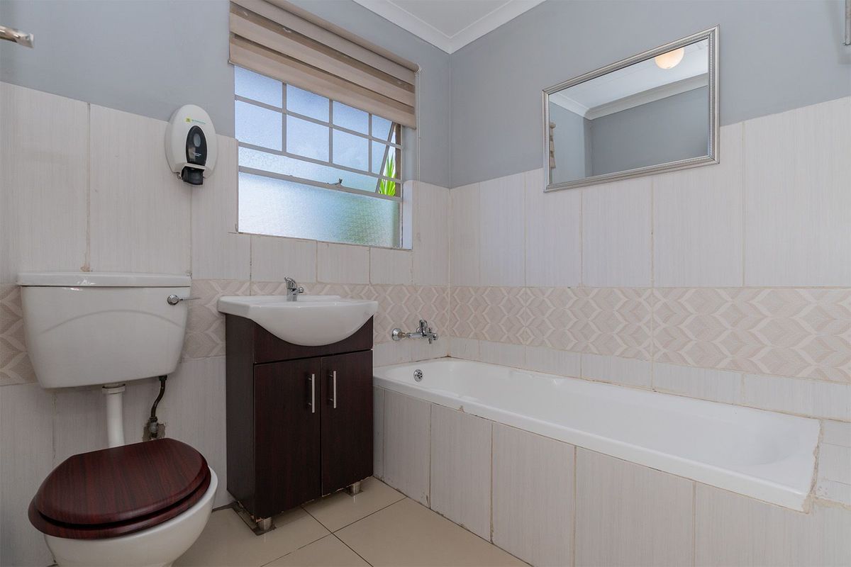 A functional bathroom featuring a built-in bathtub, vanity cabinet with basin, and toilet, finished with tiled walls and flooring.