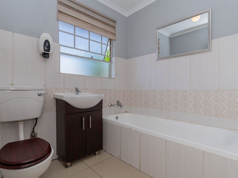 A functional bathroom featuring a built-in bathtub, vanity cabinet with basin, and toilet, finished with tiled walls and flooring.