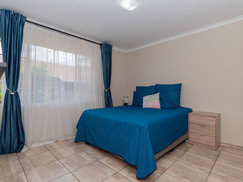 A well-lit bedroom featuring neutral wall finishes, tiled flooring, and a large window with curtain tracks, providing a comfortable and functional living space.