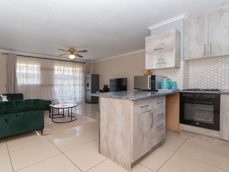 Open-plan living area featuring a modern kitchen with stone-look cabinetry, tiled flooring, and a seamless transition to the lounge space.