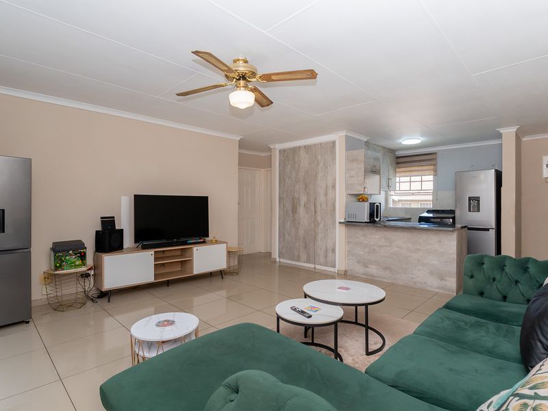 Open plan living area featuring tiled flooring, a ceiling fan, and a compact kitchen with a breakfast counter.