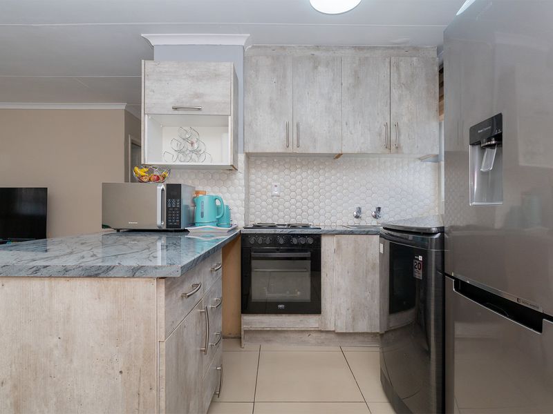 Compact kitchen featuring light wood-look cabinetry, stone-effect countertops, a built-in oven with hob, and a modern hexagonal tile backsplash.