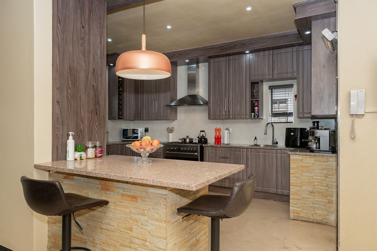Modern kitchen featuring dark wood cabinetry, granite countertops, a stone-clad breakfast island, stainless steel extractor fan, and recessed ceiling lighting.