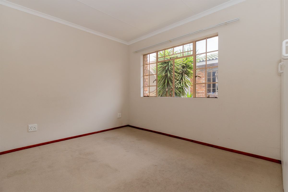 A clean, empty bedroom featuring neutral walls, carpeted flooring, and a large window providing natural light.