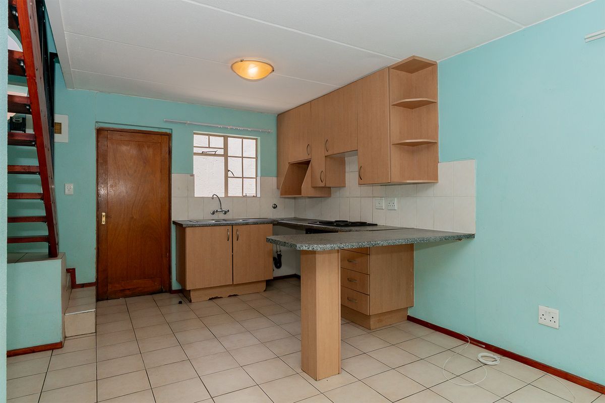 A functional kitchen featuring light wood cabinetry, a breakfast bar, tiled flooring, and a built-in hob, adjacent to an internal staircase.