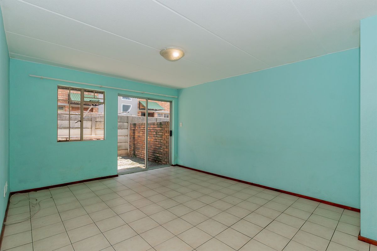 An empty living room featuring light blue walls, tiled flooring, and a sliding glass door providing access to a small paved outdoor area.