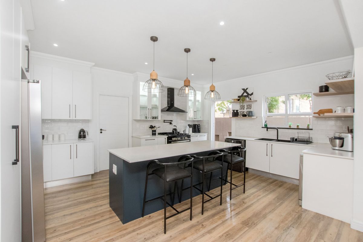 Modern kitchen featuring white cabinetry, a contrasting dark central island with breakfast bar seating, subway tile backsplash, and integrated stainless steel appliances.