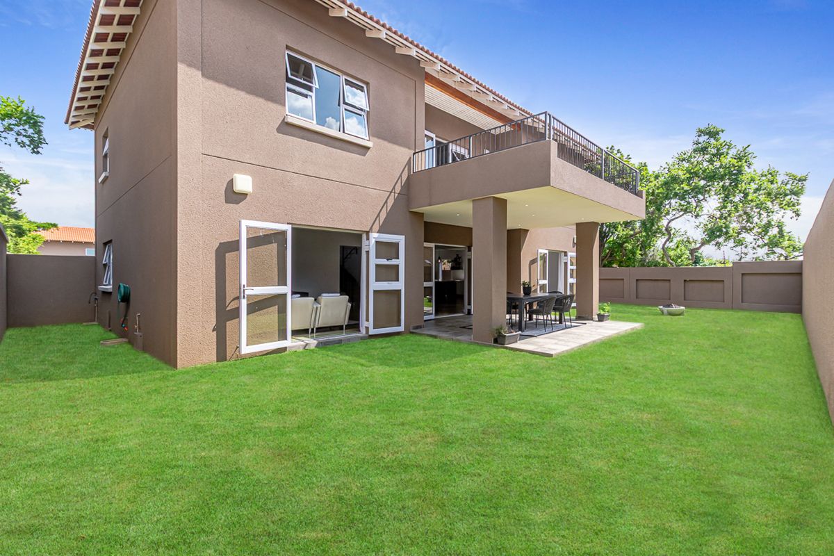Rear view of the house featuring a covered patio, upper balcony with metal railing, and a well-maintained lawn.