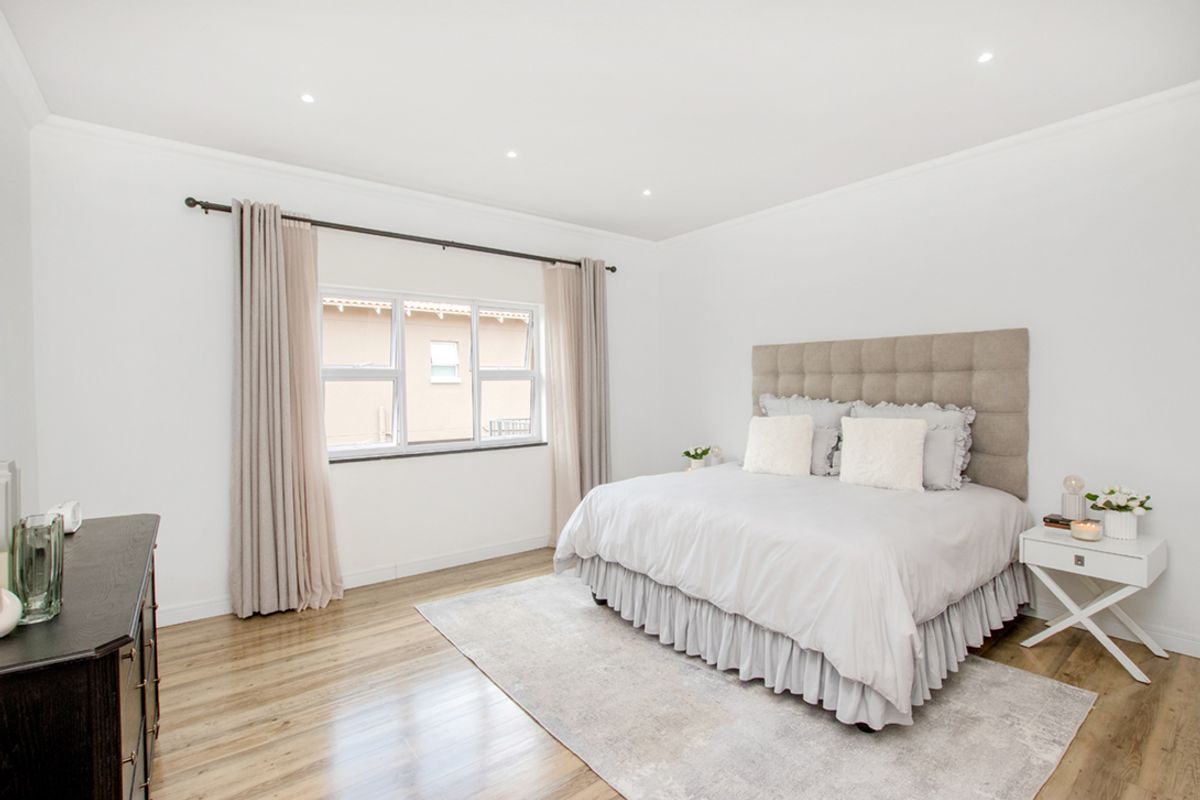 A bright and spacious bedroom featuring neutral tones, recessed ceiling lighting, and light-toned wood flooring.