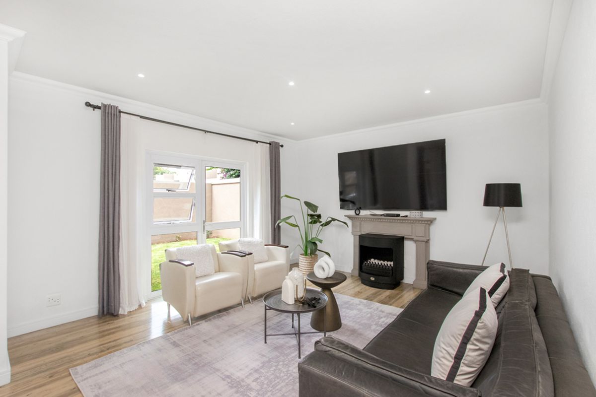 A bright and modern living room featuring wood-look flooring, recessed lighting, a decorative fireplace mantel, and glass sliding doors leading to the garden.