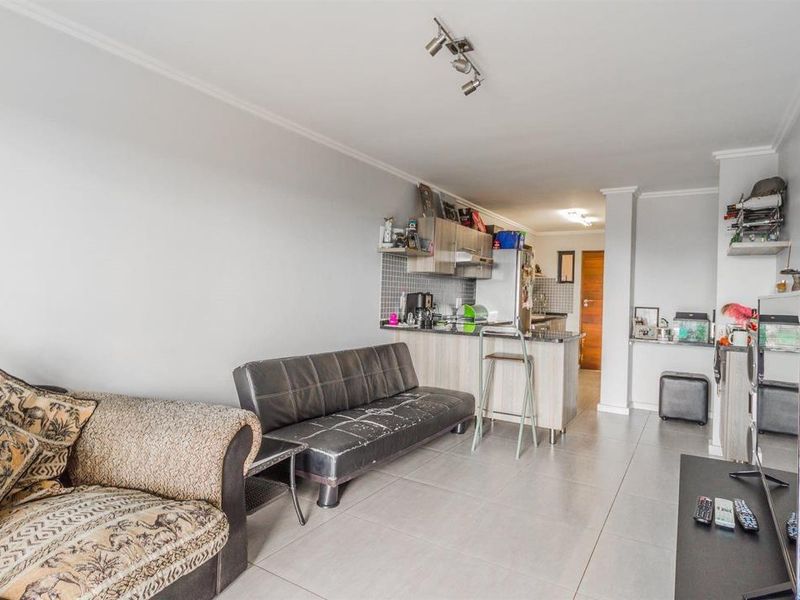 Open-plan living area featuring tiled flooring and a compact kitchen with built-in cabinetry and a breakfast counter.