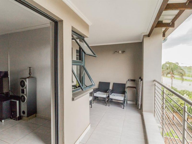 A covered balcony featuring tiled flooring, a stainless steel balustrade, and direct access to the interior living area through a sliding door.