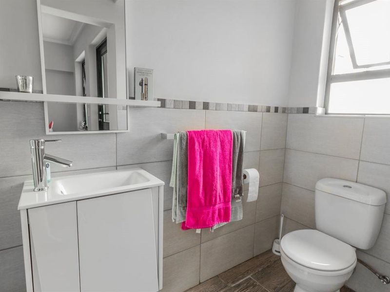A clean and functional bathroom featuring a modern vanity cabinet, basin, wall-mounted mirror, toilet, and neutral wall tiling with a decorative border.