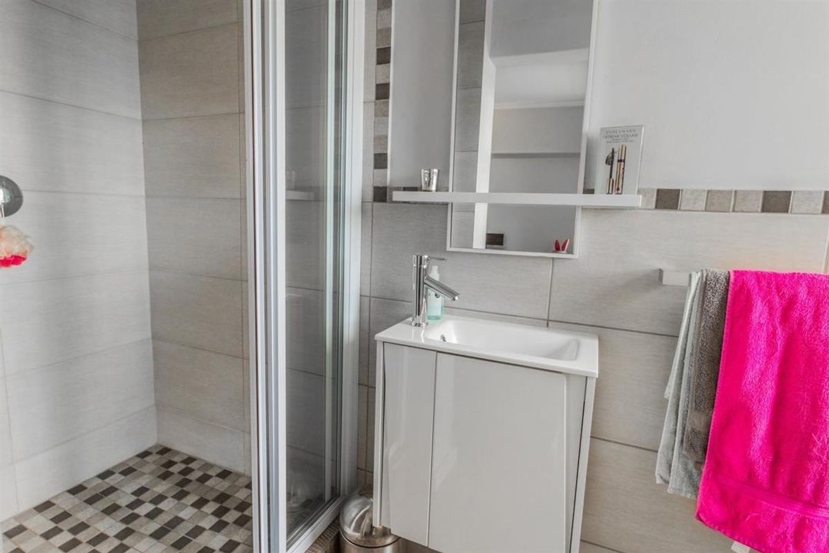 Modern bathroom featuring a glass shower enclosure, a compact vanity unit with basin, and neutral wall tiling with mosaic floor accents.