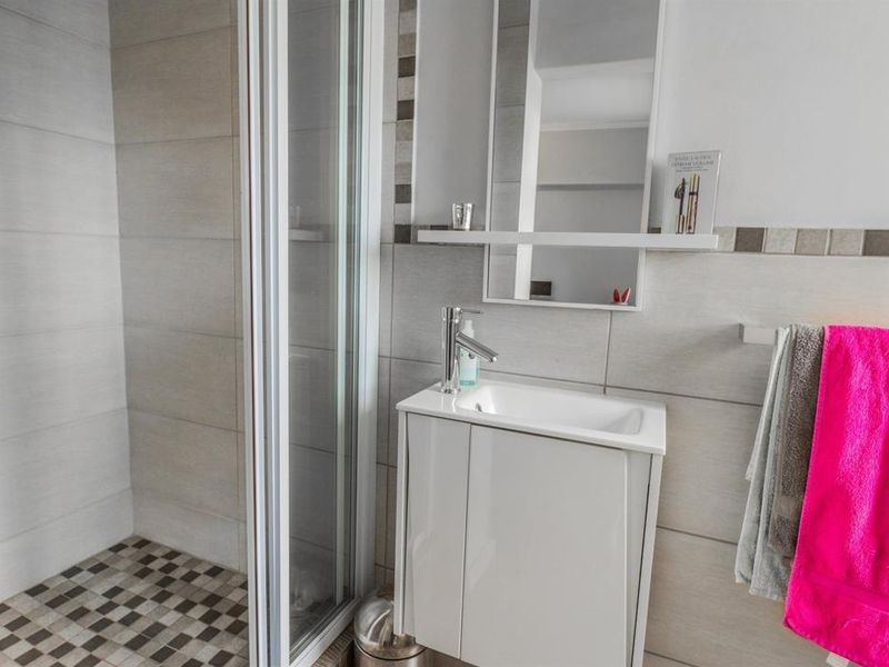 Modern bathroom featuring a glass shower enclosure, a compact vanity unit with basin, and neutral wall tiling with mosaic floor accents.