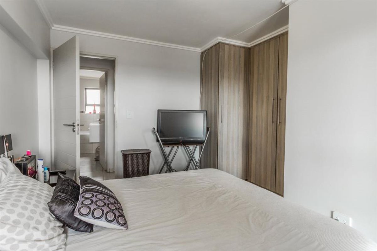 A bedroom featuring built-in wooden cupboards and access to an adjoining bathroom, finished with simple coving and neutral wall tones.